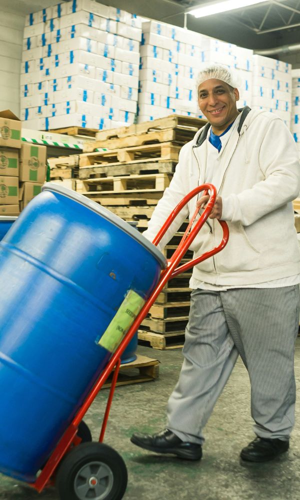 Employé logistique transportant un fût bleu sur diable